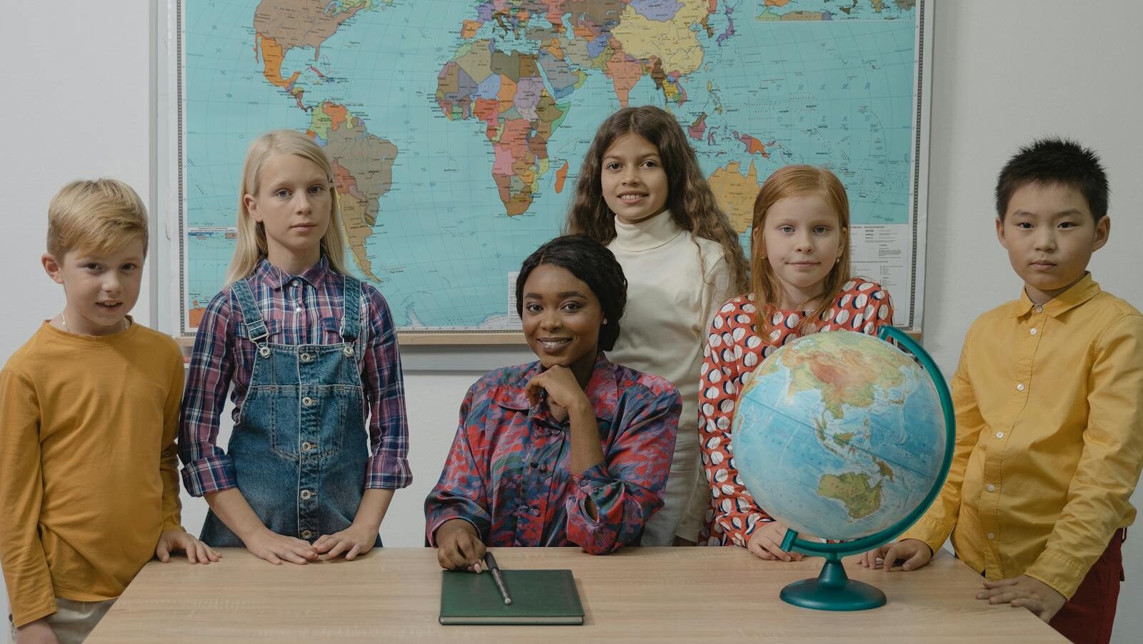 Teacher and a Group of Children Standing Beside Table With Globe